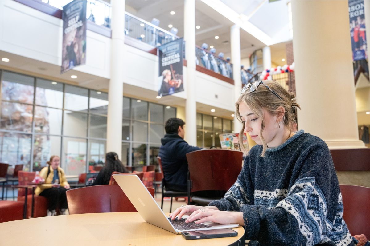 Girl works at her computer with her phone by her side at a table