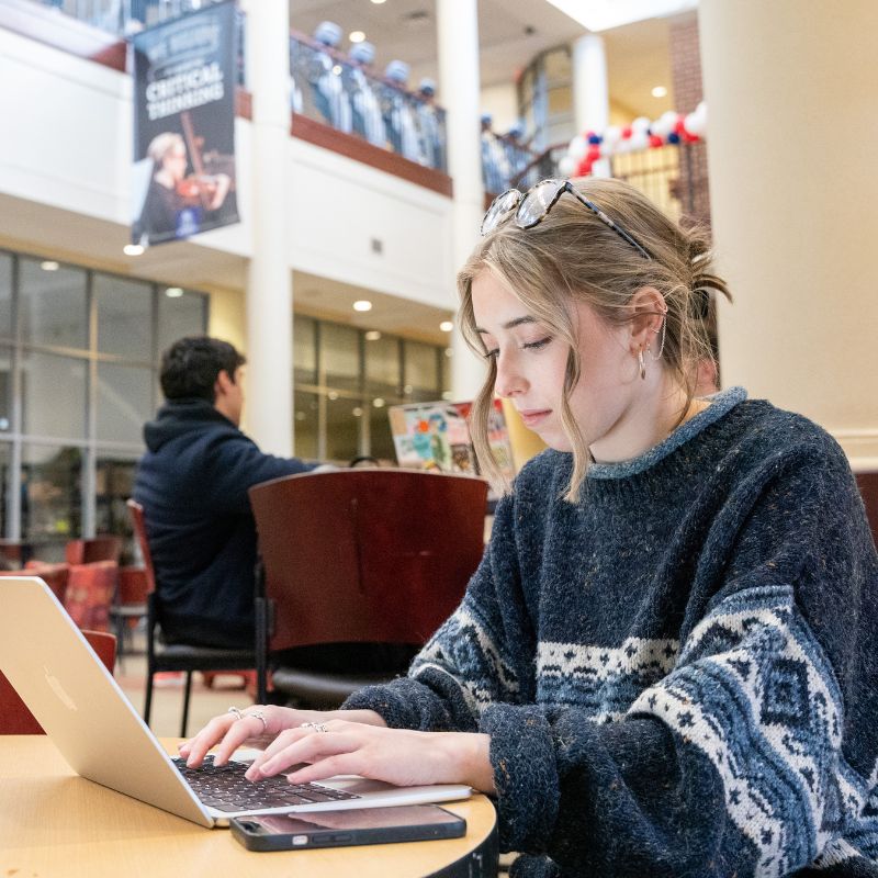 Girl works at her computer with her phone by her side at a table