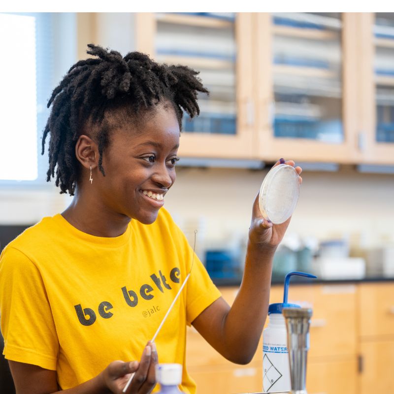 Girl smiles while holding up dish at camp