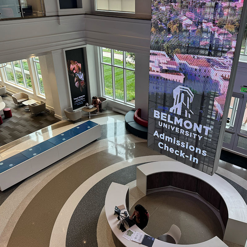 Interior view of the Admissions Welcome Center at Belmont University, featuring a large digital screen displaying 'Belmont University Admissions Check-In' and a reception desk in the foreground.