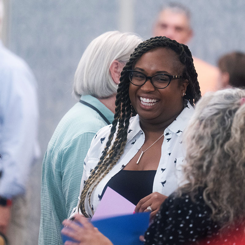 A woman smiling and engaging in conversation with others during a social event or gathering.