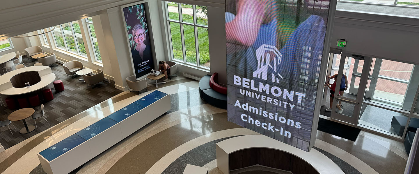 Interior view of the Admissions Welcome Center at Belmont University, featuring a large digital screen displaying 'Belmont University Admissions Check-In' and a reception desk in the foreground.