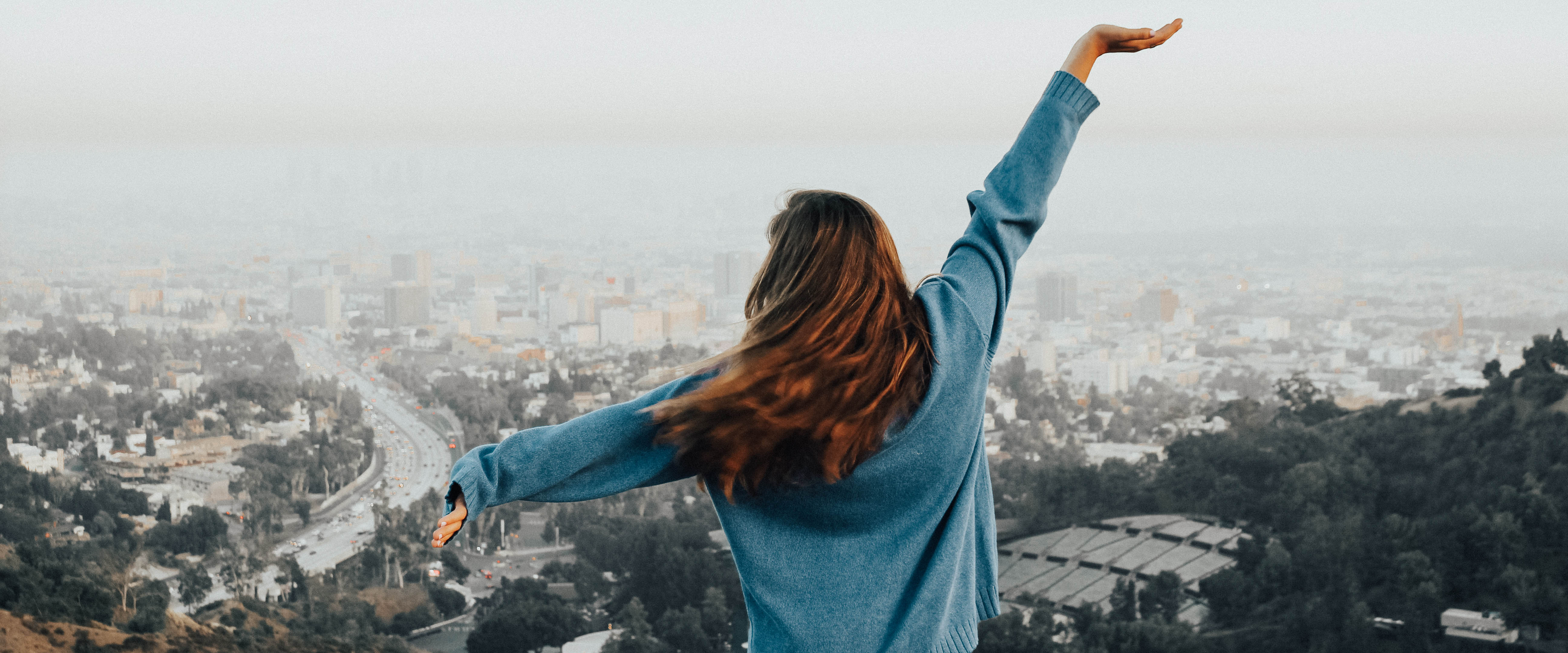 Belmont USA student poses with her arms out while facing the city of Hollywood on a hill