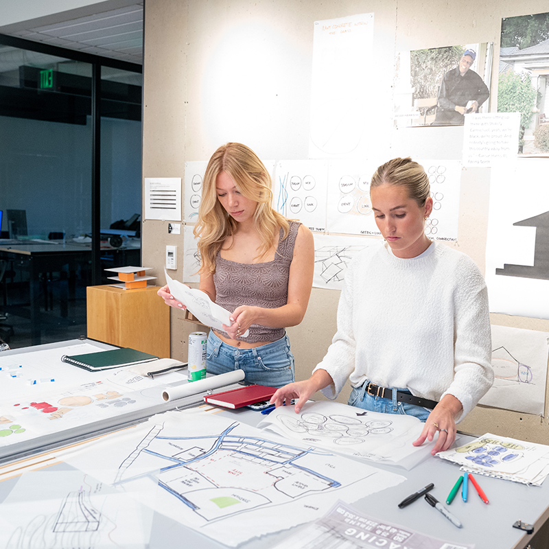 Two students looking at architectural drawing on a table