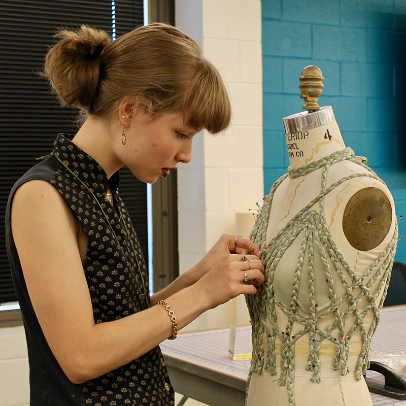 student braiding chords over a dress form