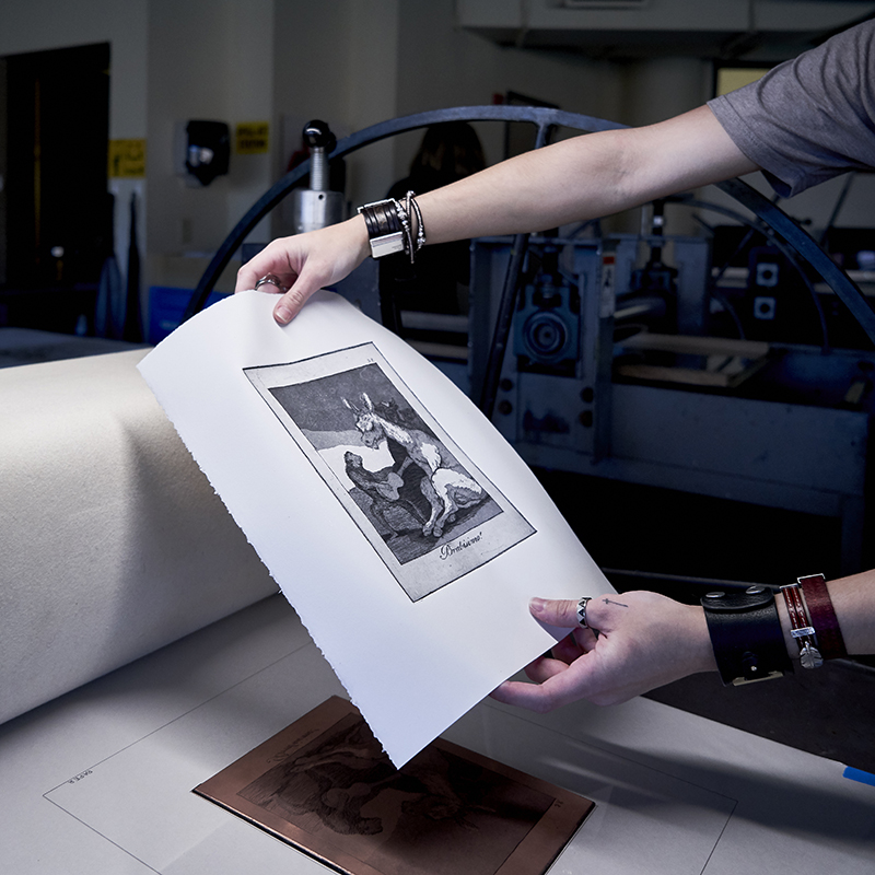 A student takes off a freshly inked print from a copper etching plate.