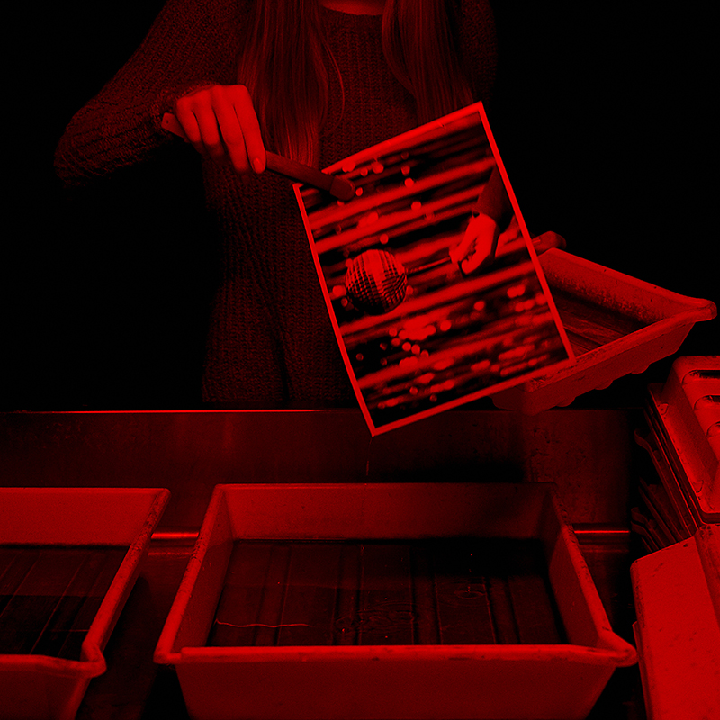 hands holding photographs with tongs over a rinsing tray